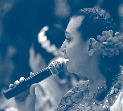 A Latina woman with a flower in her hair speaking into a microphone