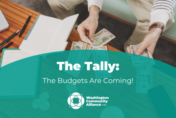 A stock photo of a white person at a table with a computer, pens, paper, and cash in front of them. A green semi-circle is overlayed with white text that reads "The Tally: The Budgets Are Coming!" and includes the WCA logo.